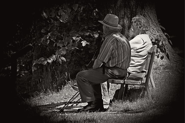 grayscaled photo of man and woman sitting on wooden outdoor bench