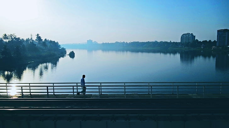 man standing on the bridge facing body of water
