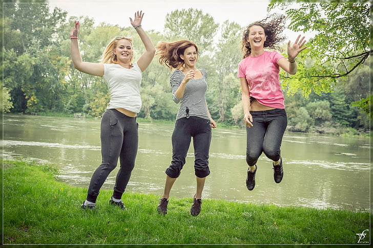 three woman jumping beside body of water