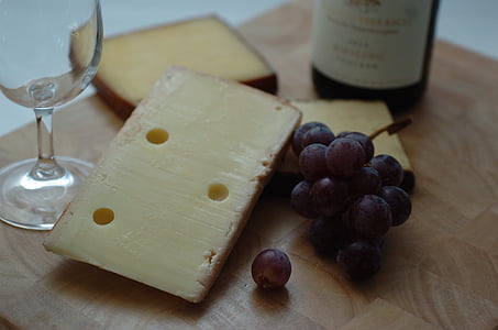 grapes beside cheese beside wine glass and bottle on wooden surface