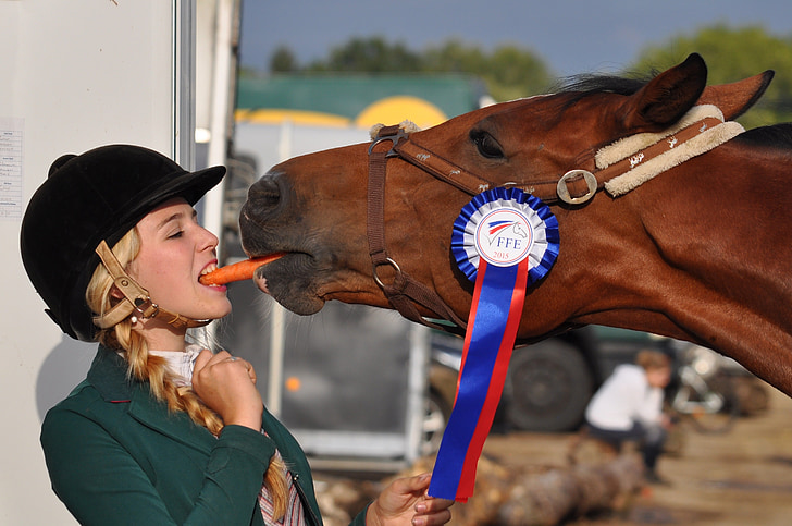 woman biting carrot with horse