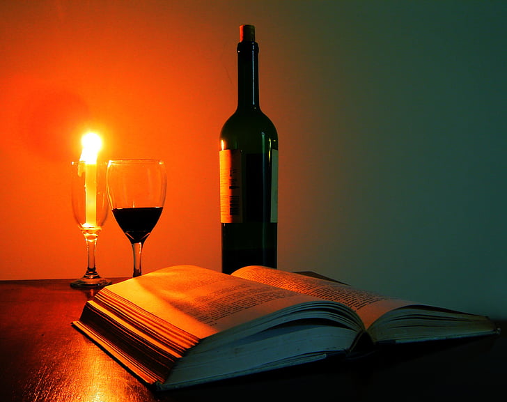 black glass bottle beside wine glasses filled with liquid and candle
