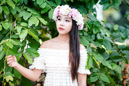 woman wearing flower headdress and off-shoulder dress standing next to leafy plant
