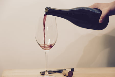 closeup photo of person holding liquor bottle near wine glass