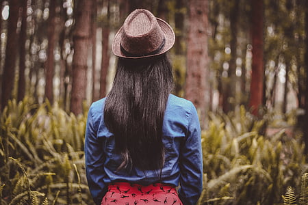 woman wearing blue jacket and red bottoms with fedora hat in woods