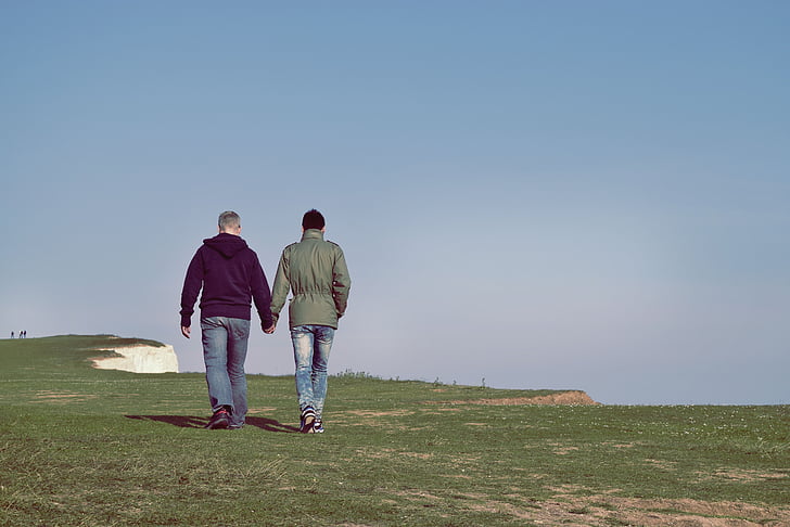 two person walking on green grass holding both hands during daytime
