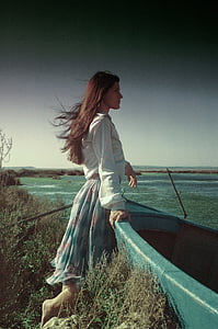 woman in white shirt and blue floral skirt holding plastic boat facing ocean