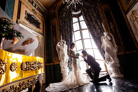 groom kneeling in front of his bride by the window