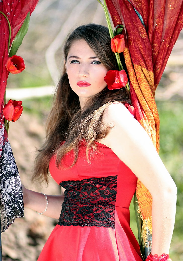 woman wearing red and black floral sleeveless dress holding curtain with flowers