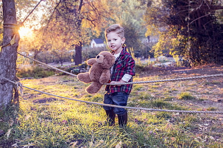 boy carrying bear plush toy holding onto a rope attached to trees