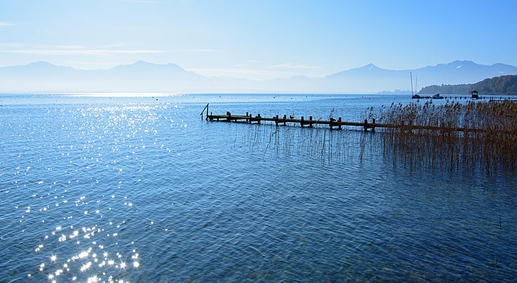 brown and black dock between body of water near mountains under white and blue sky at daytime