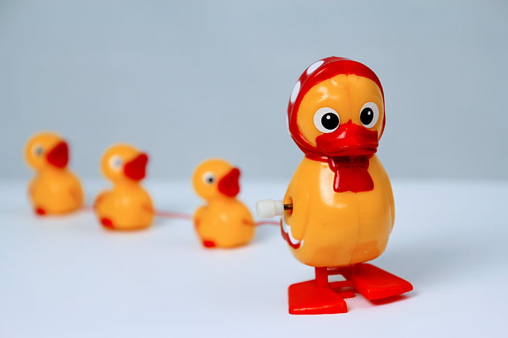 yellow and red plastic duck with 3 ducklings plastic toy on white surface