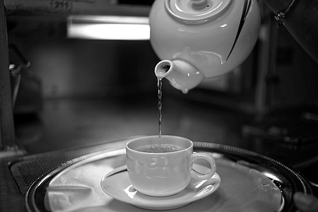 selective focus photography of water poured by pitcher unto white ceramic teacup with saucer on tray