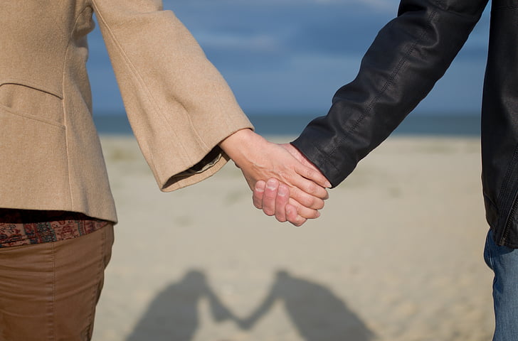 man and woman holding hands on seashore near beach