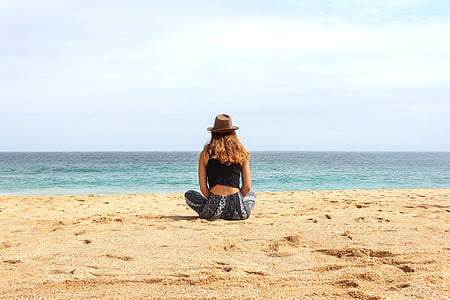 woman in black tank top sitting on seashore during daytime