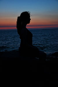silhouette photography of woman sits on rock near ocean