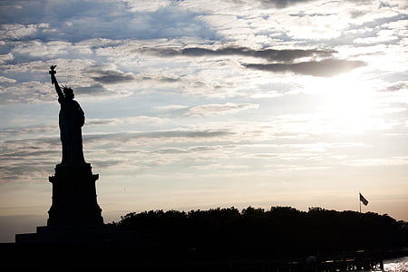 silhouette of Statue of Liberty under white clouds at golden hour