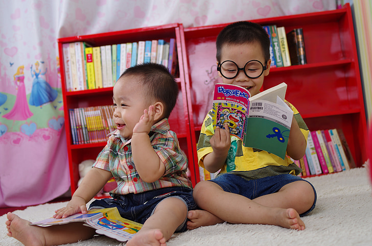 two boys reading books while sitting on floor