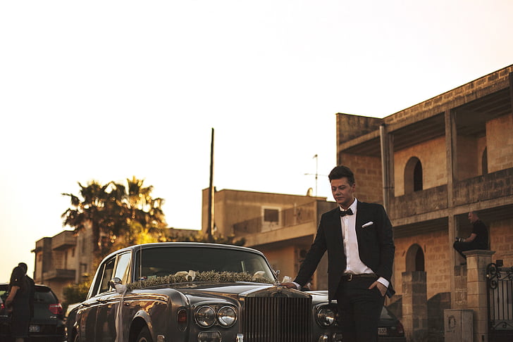 man in black tuxedo standing infront of classic car