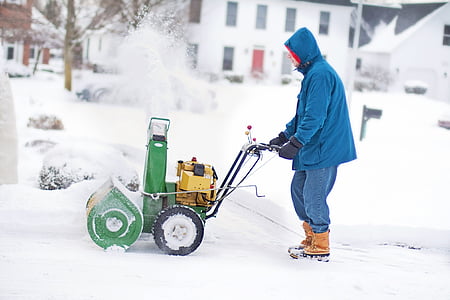 man wearing blue hooded jacket holding green snow thrower