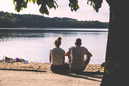 couple sitting on concrete floor front of body of water