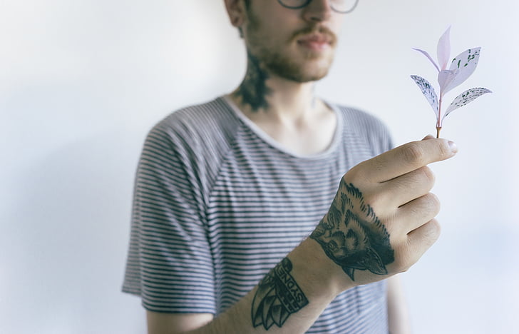 man with tattoos wearing black and white striped shirt holding white leafed plant
