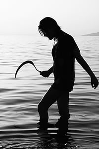 silhouette of woman holding sickle in body of water