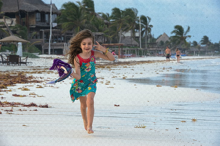 panning photography of girl holding purple textile running on seashore