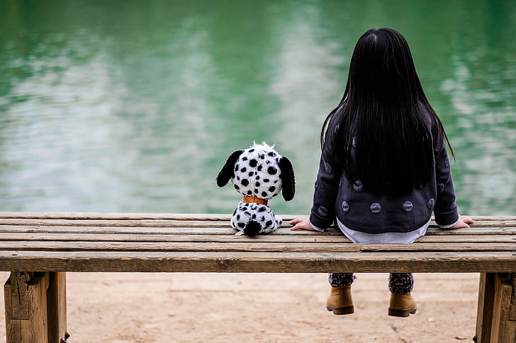 girl in black jacket and blue denim pants sitting beside dalmatian puppy plush toy during daytime