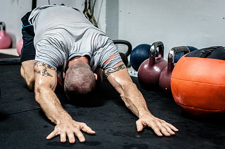 body builder laying his hands on floor near kettle dumbbells