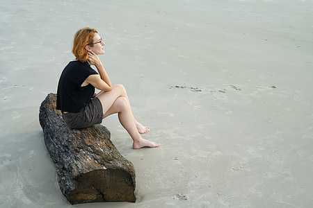 woman wearing black shorts sitting on driftwood