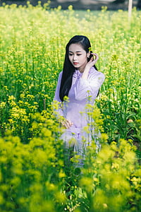 woman holding her left ear while standing in flower farm