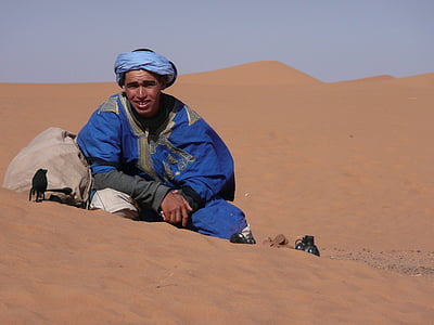 man in blue suit sitting on brown sand during daytime