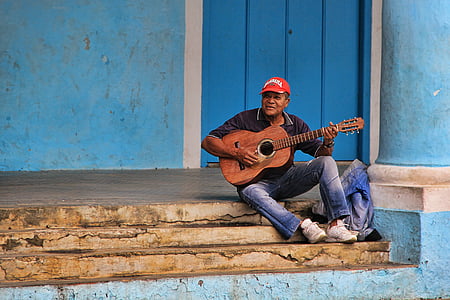 man wearing black polo shirt sitting on stairs while playing acoustic guitar