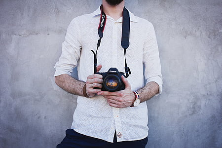 man in white dress shirt holding camera standing near wall