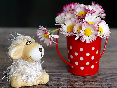daisy flowers in red and white steel pot beside ceramic sheep figurine
