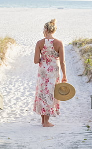 woman standing in the sand holding her hat