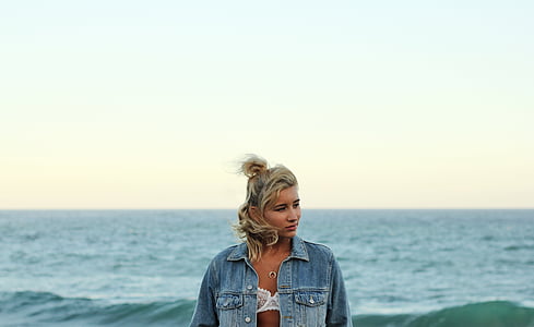 woman wearing white floral brassiere and blue denim jacket near ocean during daytime