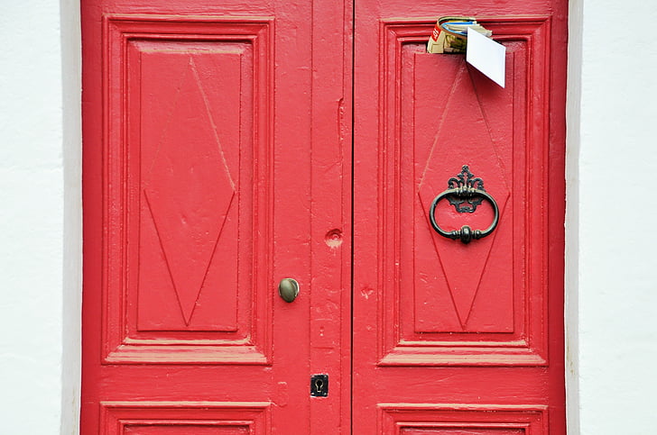 closed red wooden door with mails inserted at top