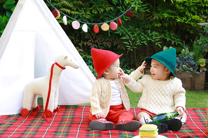 two babies sitting on red and green plaid textile