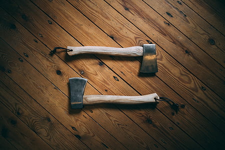 two beige wood handled axes on brown wooden surface
