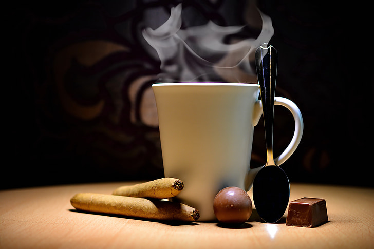 ceramic mug between spoon and cigars on table