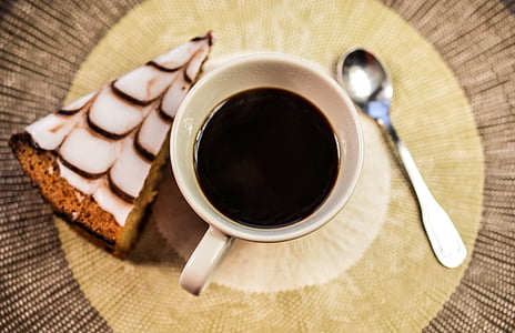 black liquid filled in white ceramic mug in between sliced cake and teaspoon