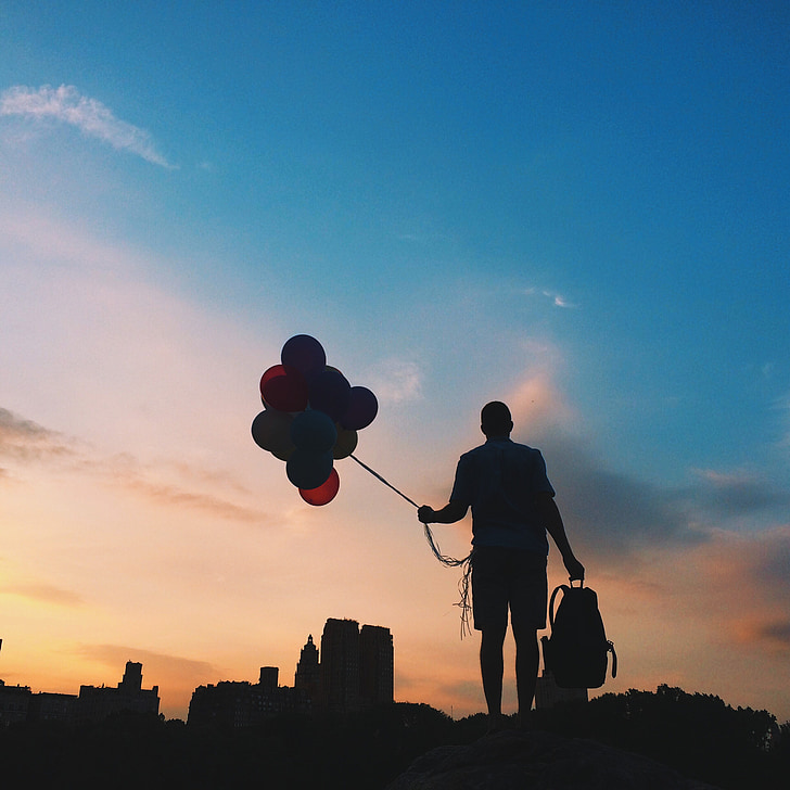 silhouette photo of person holding balloons and bag during golden hour