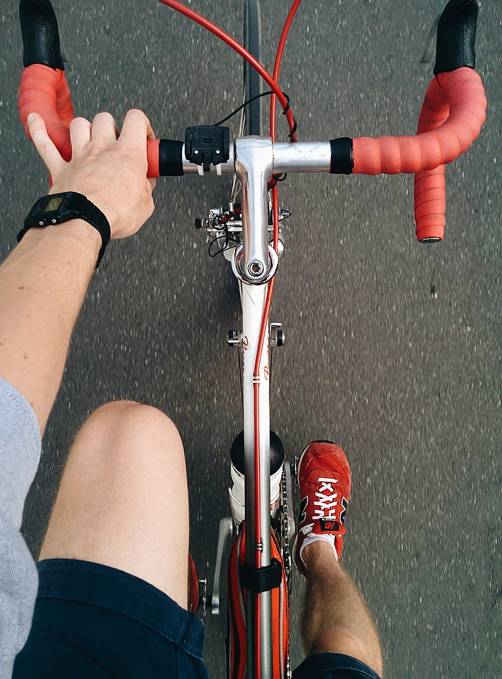 person wearing red New Balance shoes riding on road bicycle