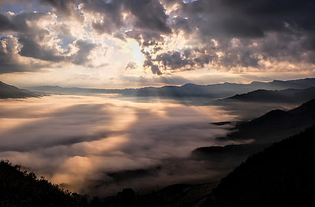 landscape photography of sea of clouds surrounded by mountains with crepuscular sun rays with cloudy sky