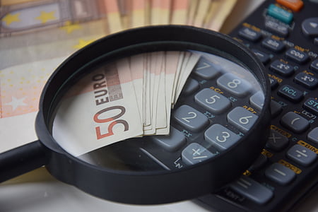 magnifying glass on top of black desk calculator and 50 Euro banknotes
