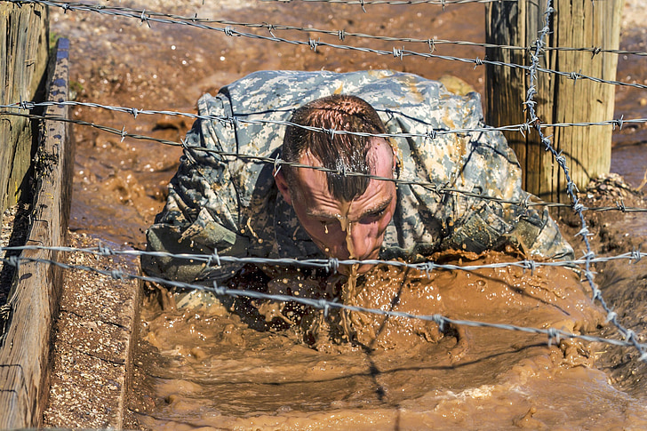 man crawling on mud under the barbwire