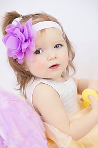 toddler girl wearing white sleeveless dress with purple and white headband looking side