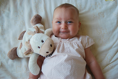 high angle photography of baby in white top laying on bed beside white cow plush toy